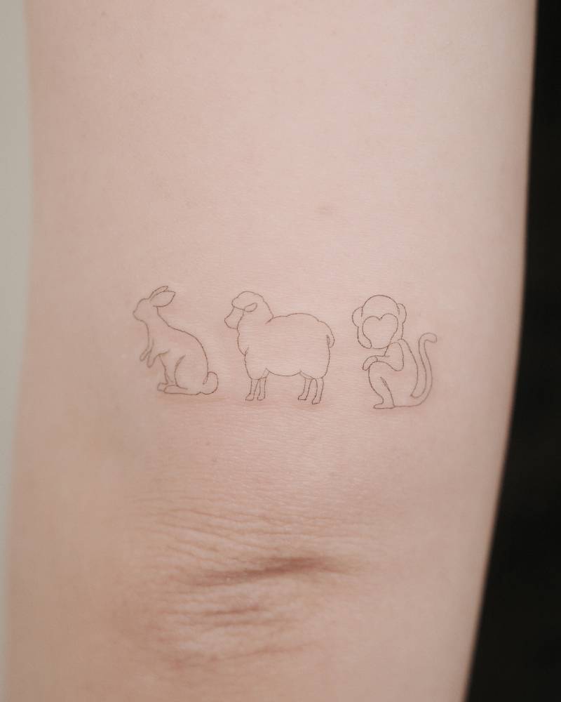 Rabbit, sheep and monkey tattoo in fine line style located on the tricep.