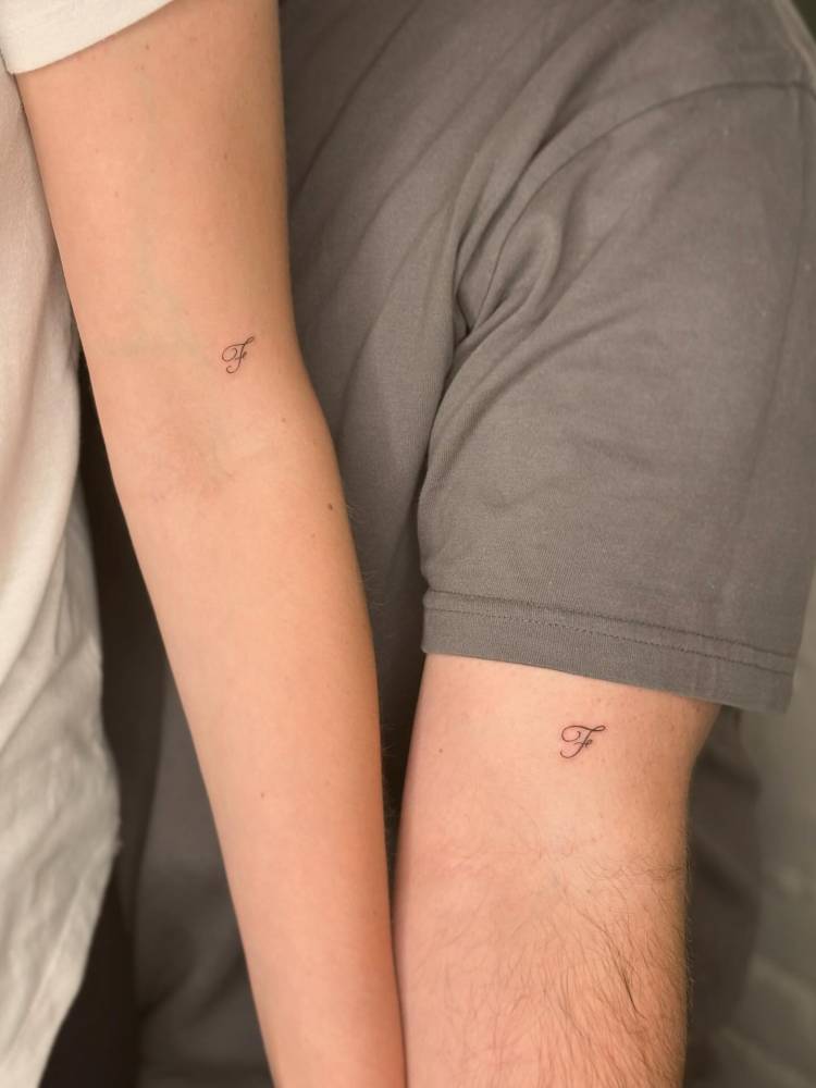 Matching script font letter "F" tattoo for couple.