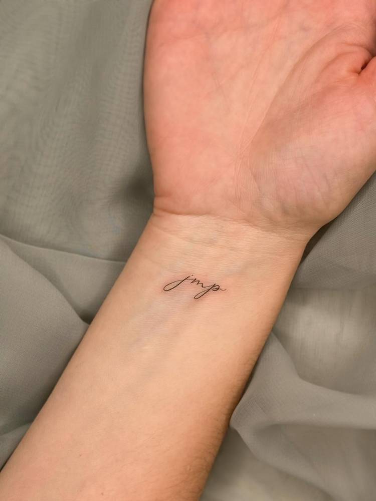 Initials tattoo in script font located on the wrist.