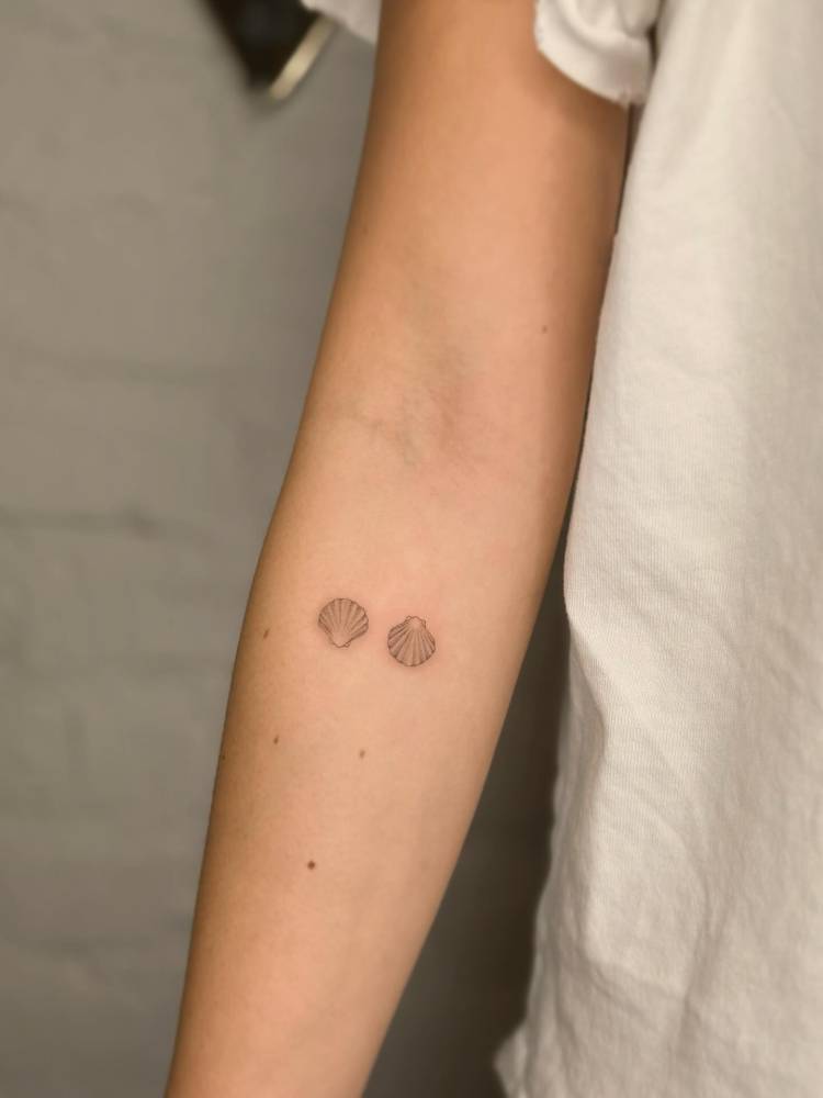 Fine line style scallop shells tattooed on the inner forearm.