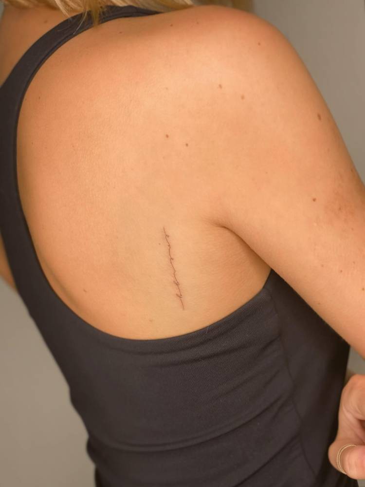 Word "energy" in handwritten font tattooed on shoulder blade.