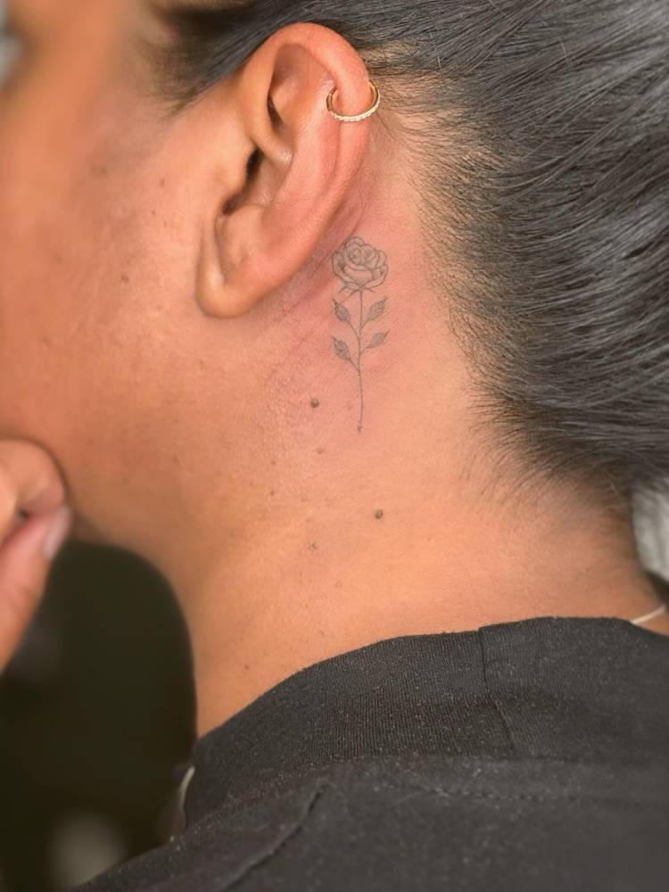 Rose tattoo in illustrative style placed behind the ear.