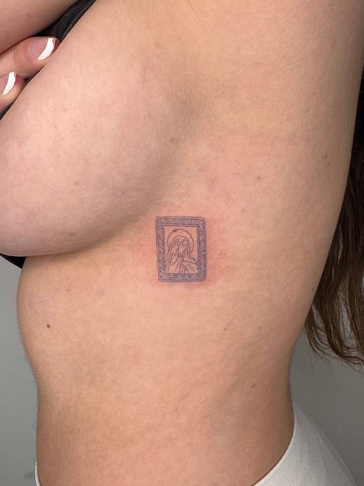 Virgin Mary picture frame tattoo located on the side boob.
