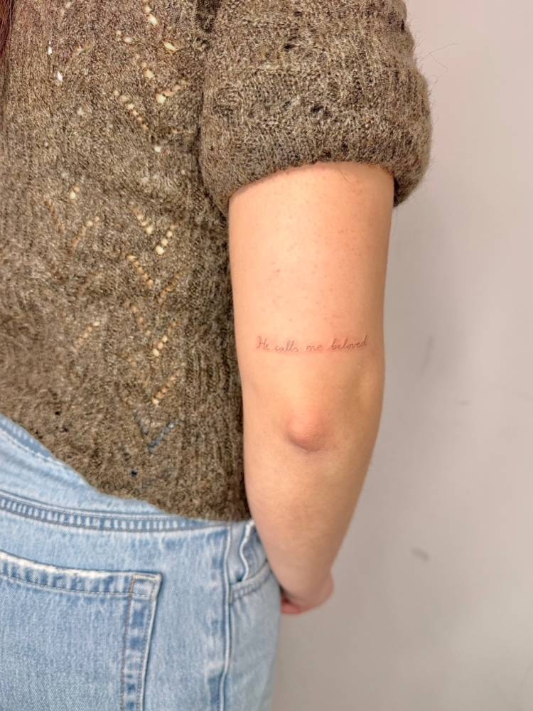 "He calls me beloved" lettering tattoo located on the tricep.