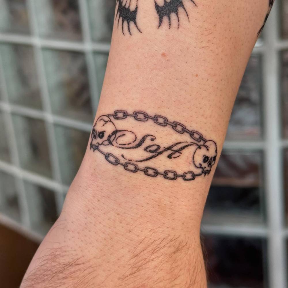 Chain and word "soft" tattoo located on the wrist.
