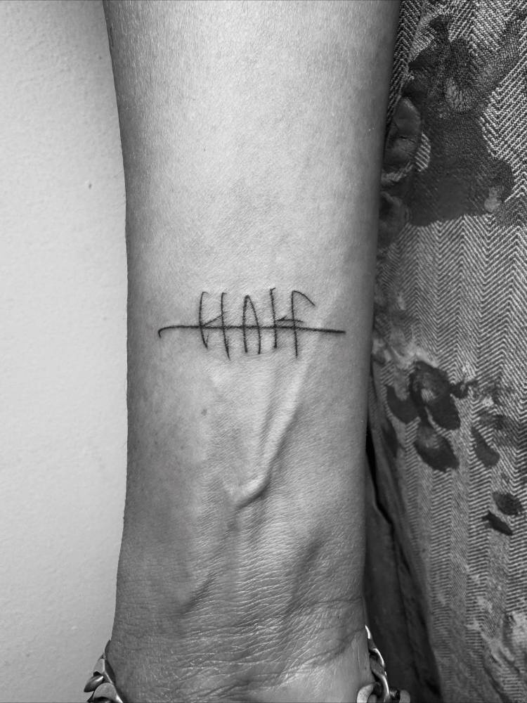 Handwritten font word "half" tattooed on the wrist.