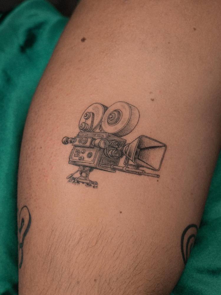 Video camera tattoo in illustrative style located on the calf.