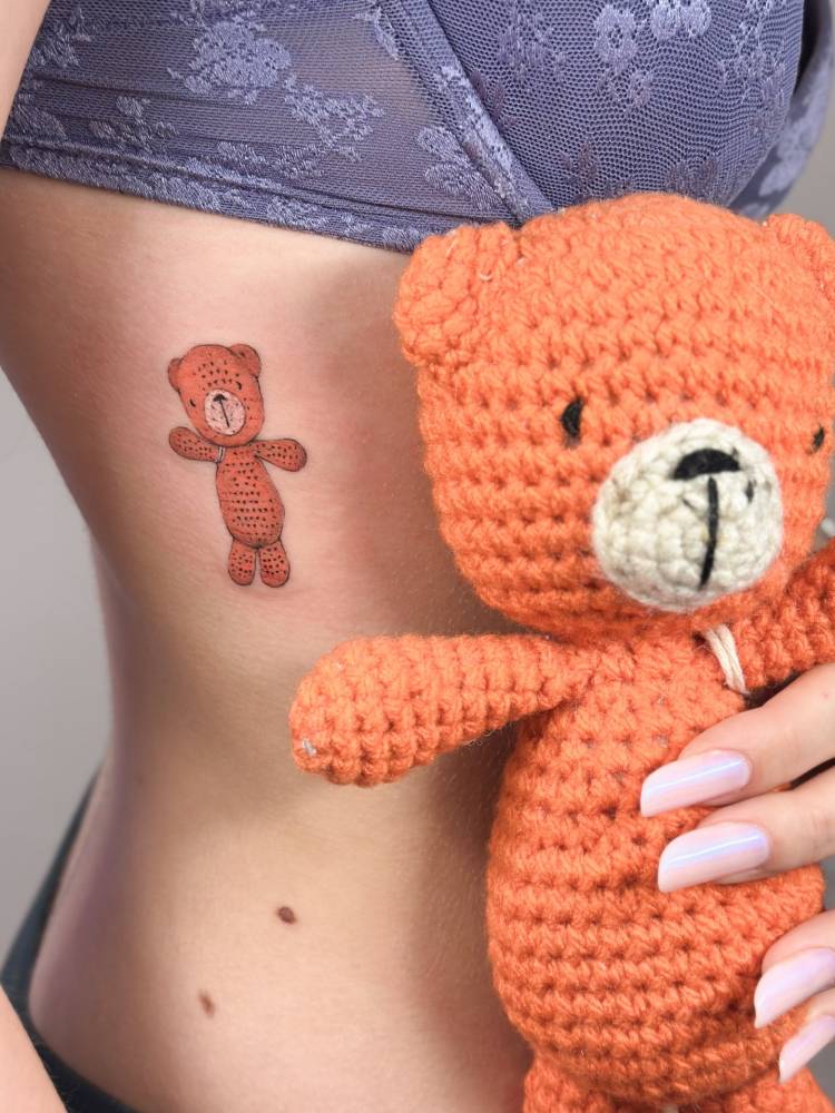 Teddy bear tattoo in cartoon style located on the rib.