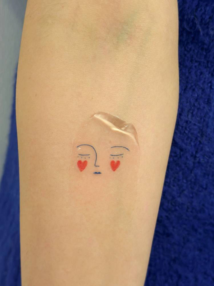 Minimalistic style face tattoo located on the inner forearm.