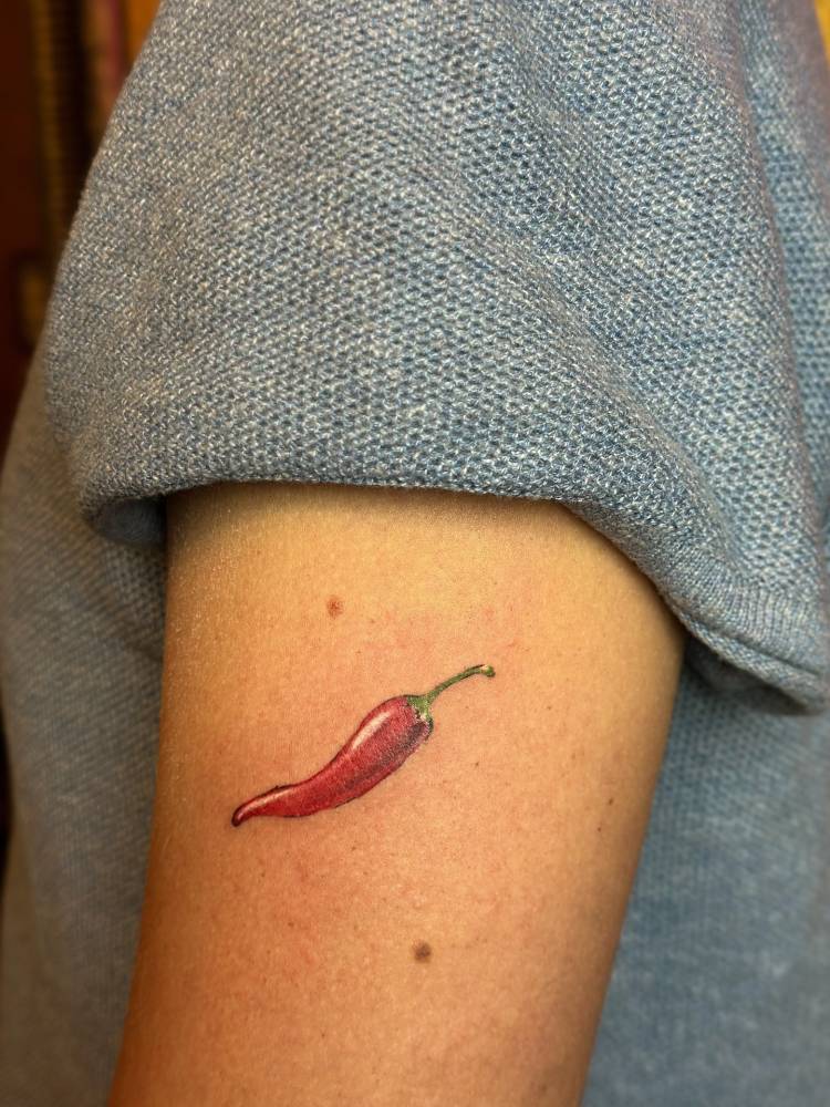 Red chili pepper tattoo located on the upper arm, done in illustrative style.