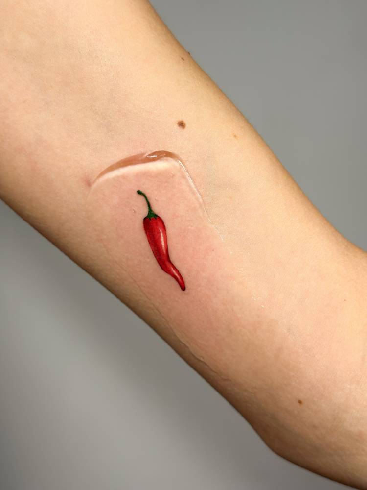 Illustrative style red chili tattoo located on the inner arm.