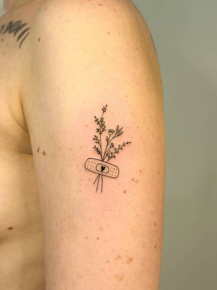 Flower bouquet and bandage tattoo located on the upper arm, fine line style.