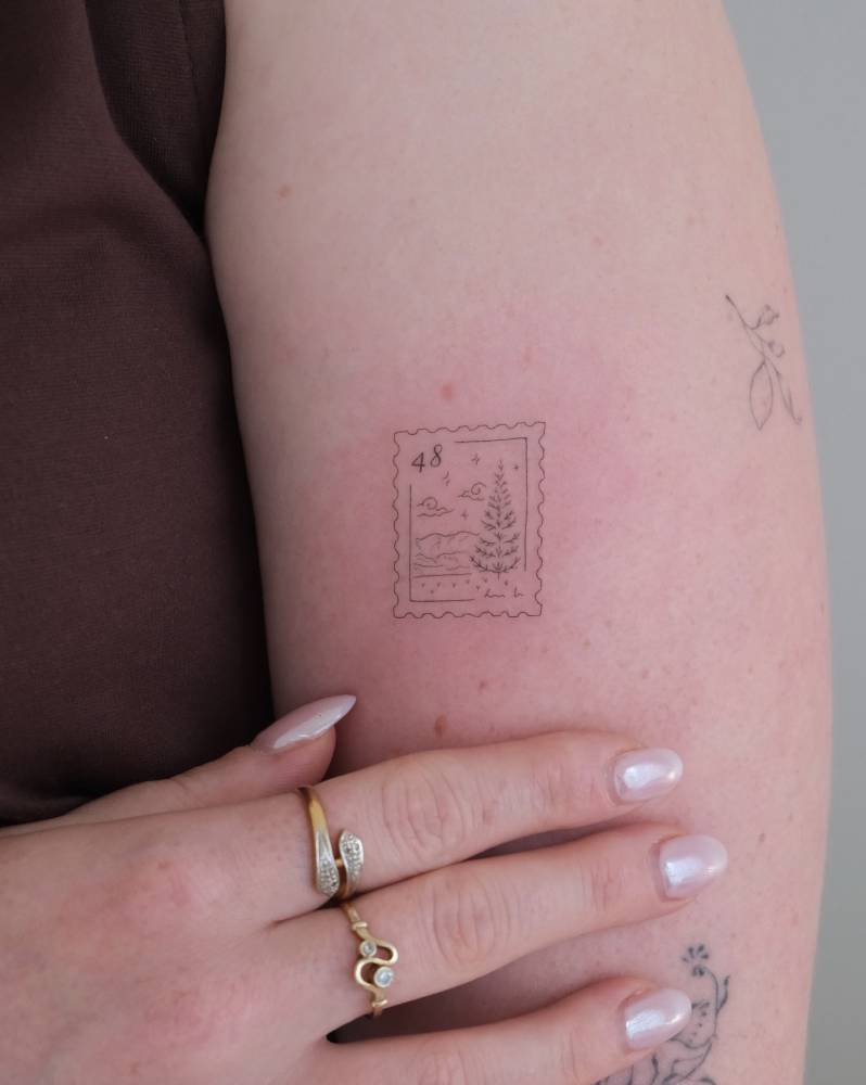Pine tree stamp tattoo in fine line style located on the upper arm.