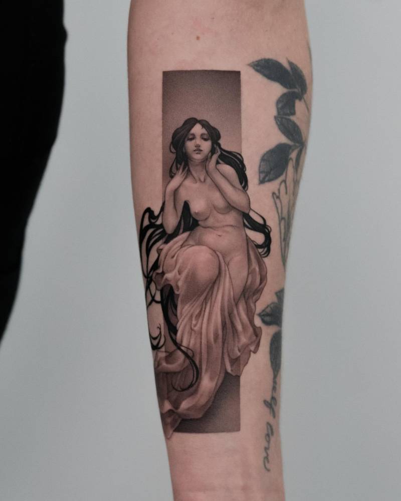 Micro-realistic style nude woman tattoo located on the inner forearm.
