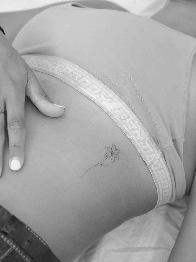 Little fine line style lily flower tattoo placed on the rib.