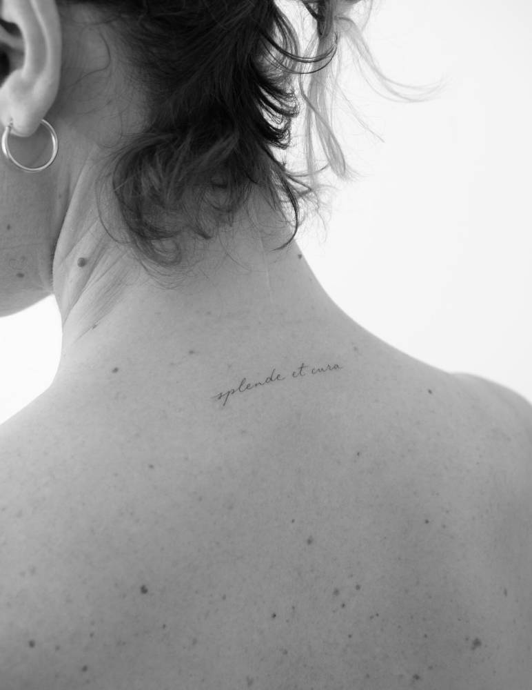 "Splende et cura" lettering tattoo handwritten on the upper back.