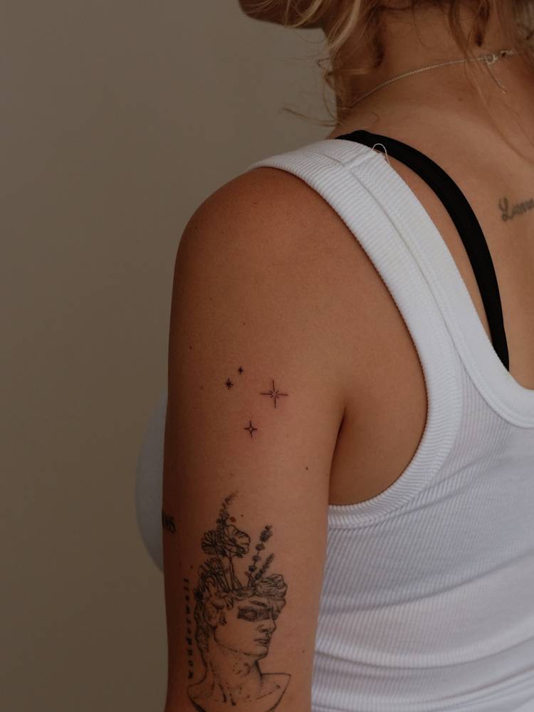 Sparkling stars tattoo located on the upper arm, fine line style.