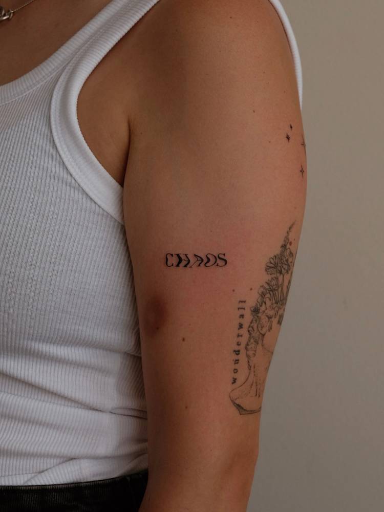 Word "chaos" tattoo located on the upper arm.
