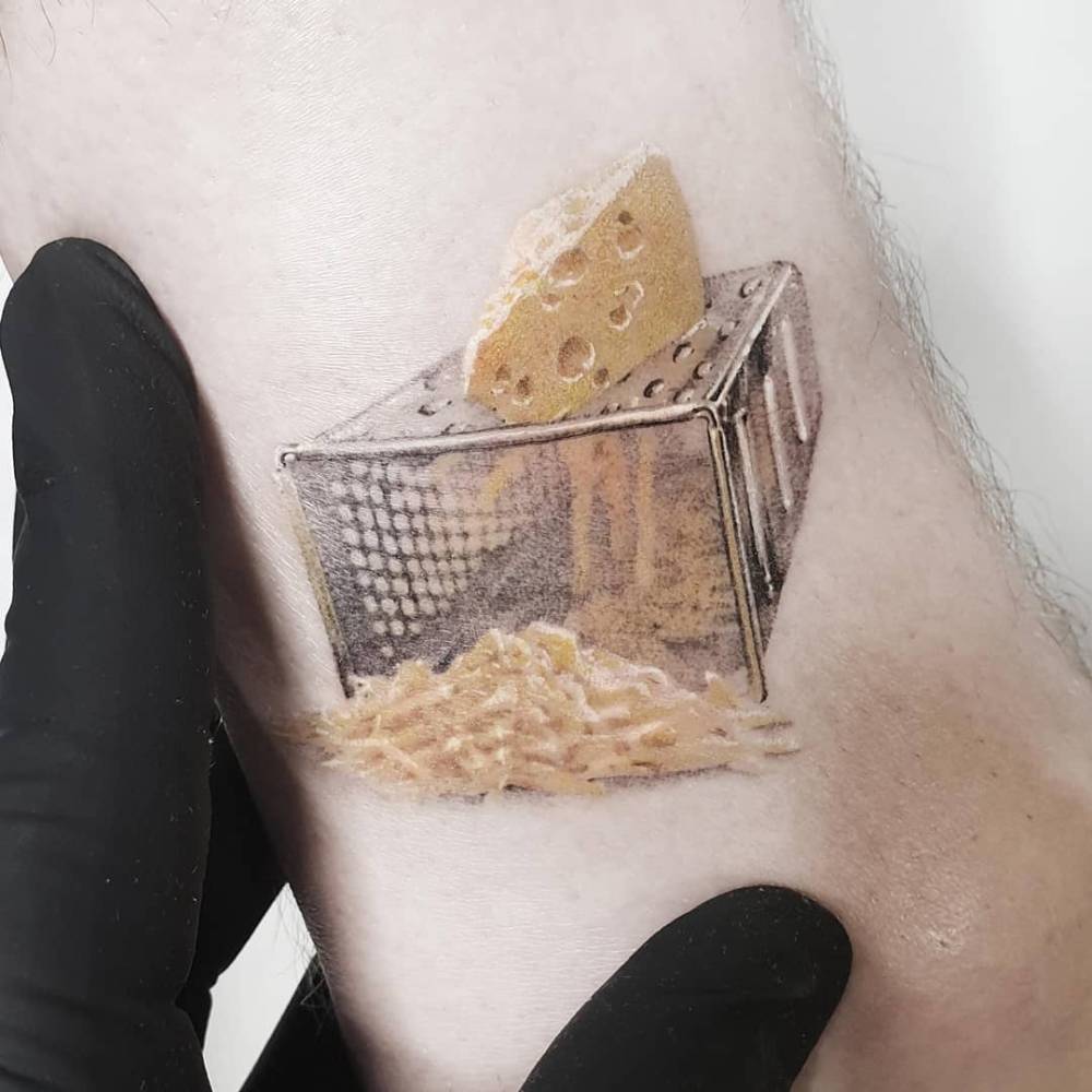 Cheese grater tattoo located on the inner arm, micro-realistic style.