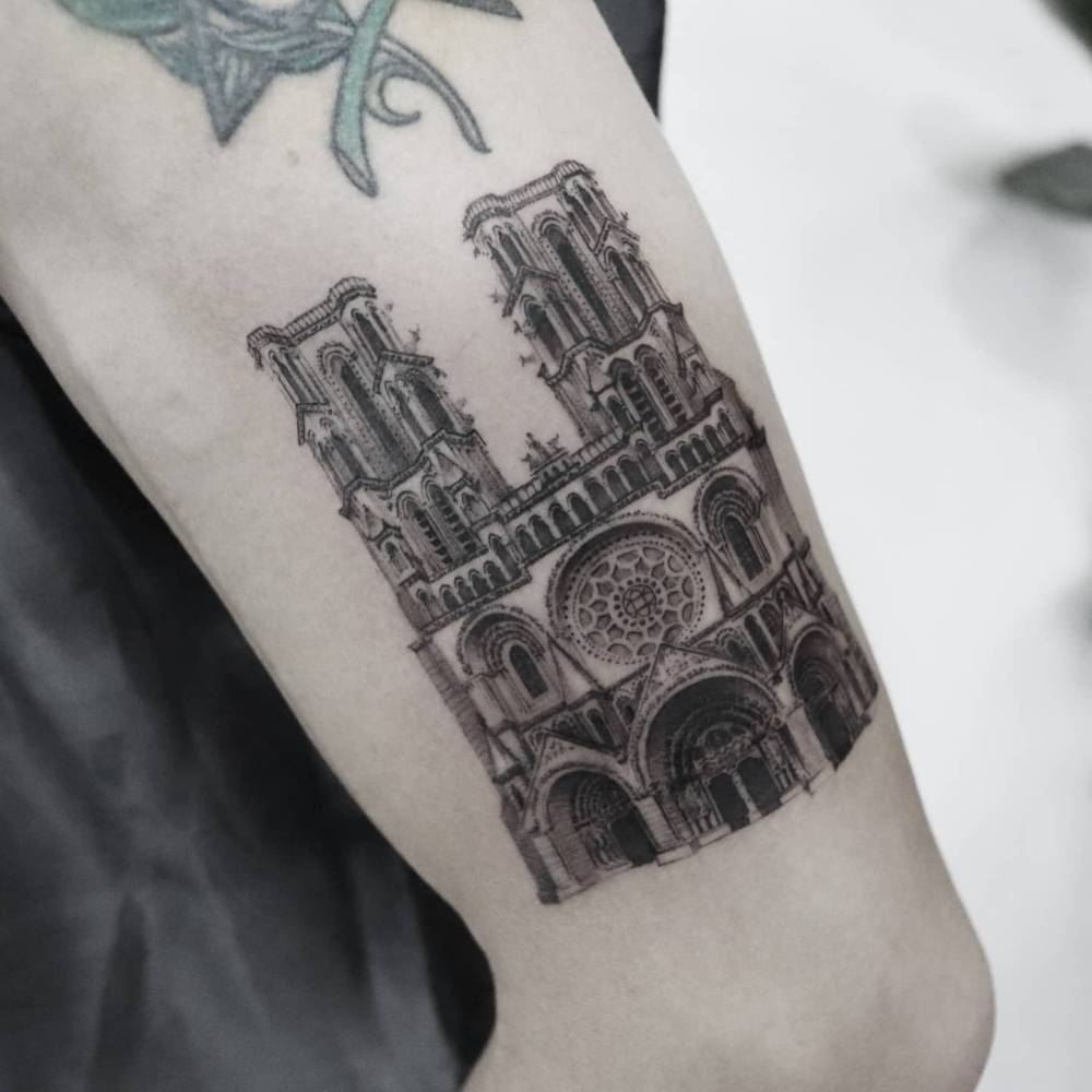 Notre-Dame Cathedral tattooed on the upper arm, micro-realistic style.