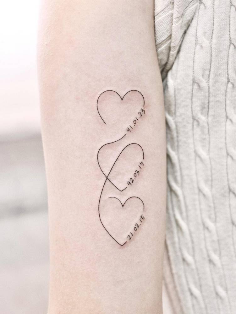Hearts and birthdates tattooed on the inner forearm, fine line style.