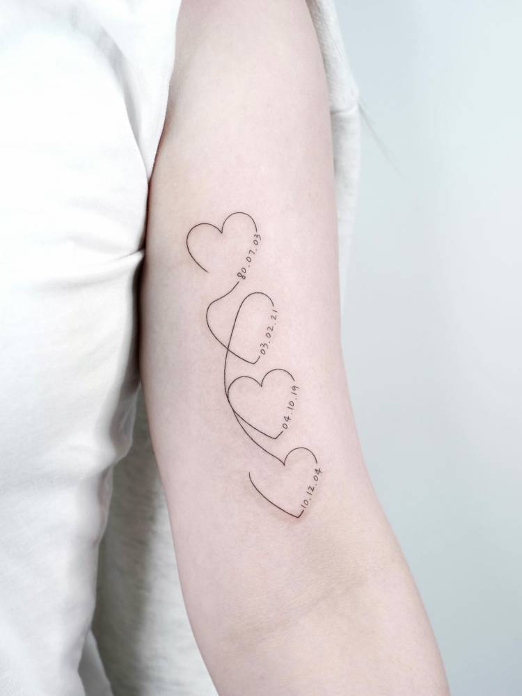 Hearts and birthdates tattooed on the bicep, fine line style.