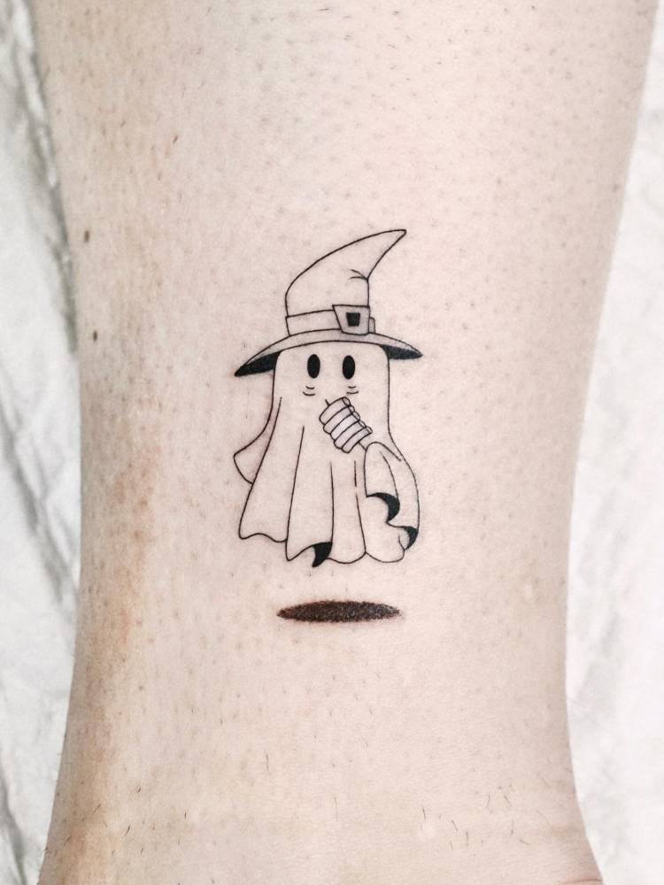 Cartoon style ghost wearing a witch hat tattooed on the ankle.
