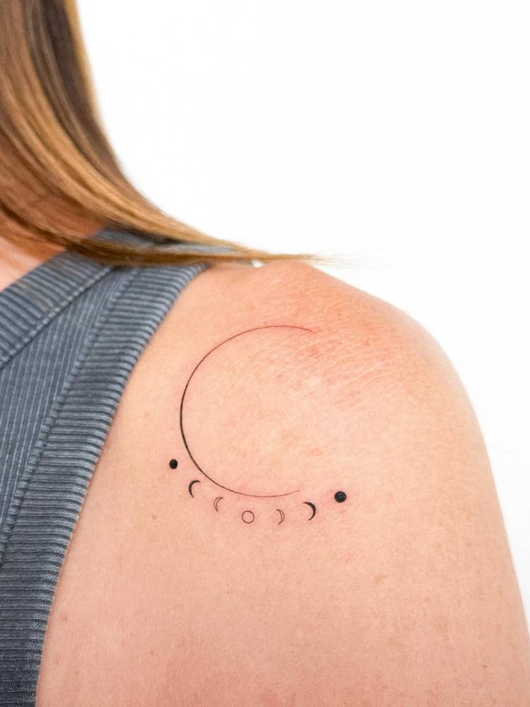 Minimalistic style moon phases tattoo located on the shoulder.