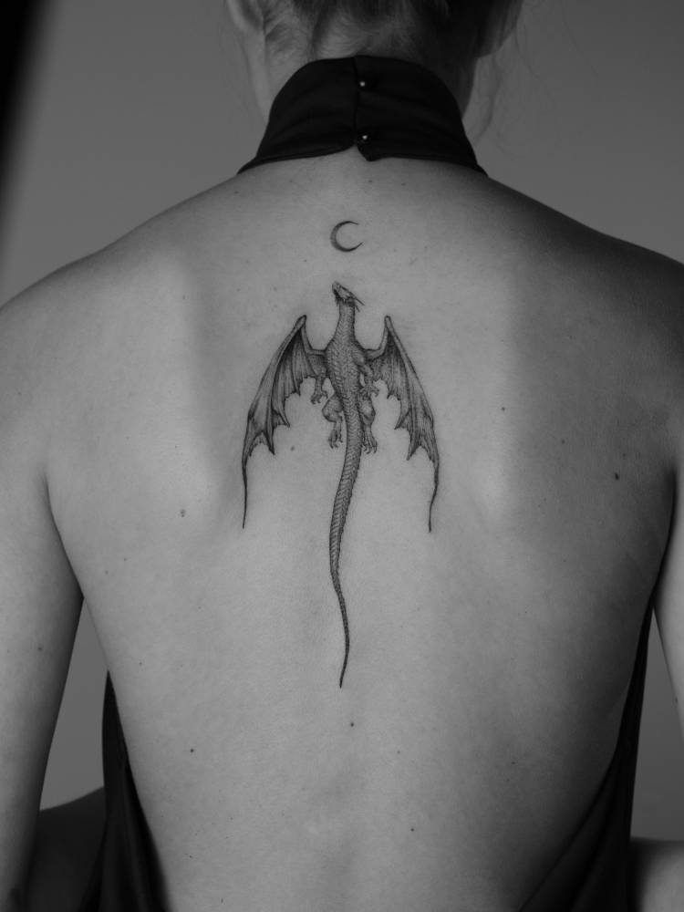 Dragon tattoo in illustrative style located on the upper back.