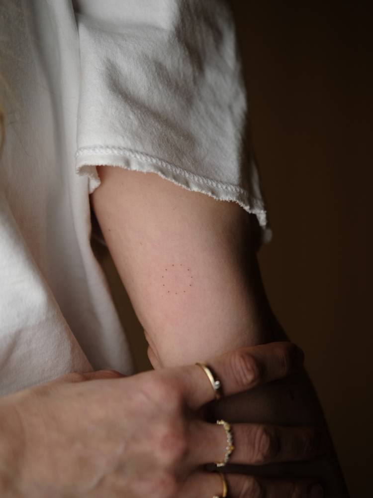Tiny dotted circle tattooed on the inner arm, minimalistic style.