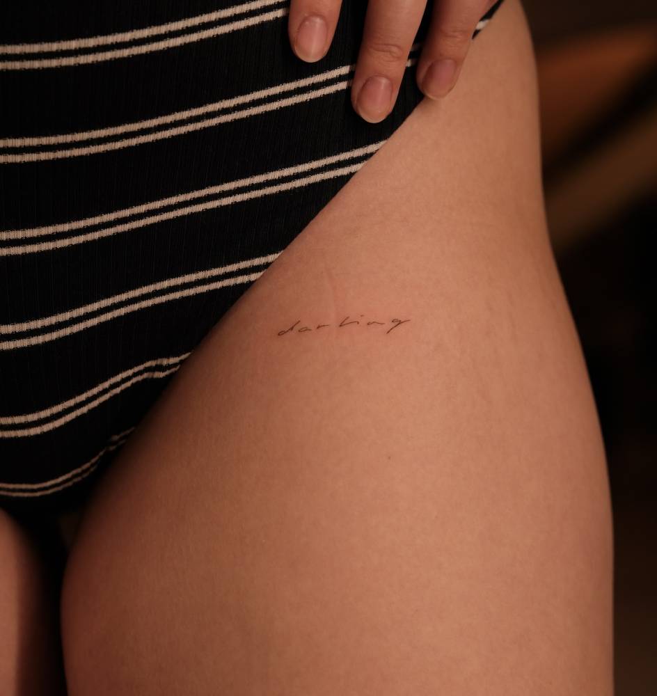 Handwritten font word "darling" tattooed on the pelvis.