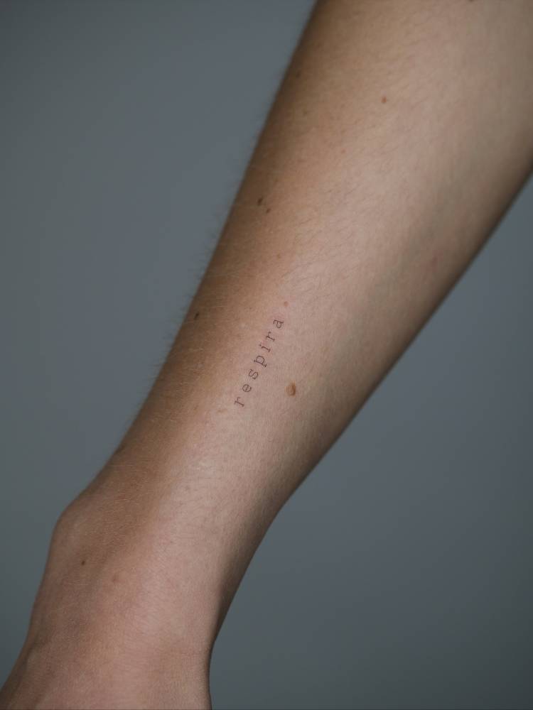 "Respira" lettering tattoo in typewriter font located on the wrist.