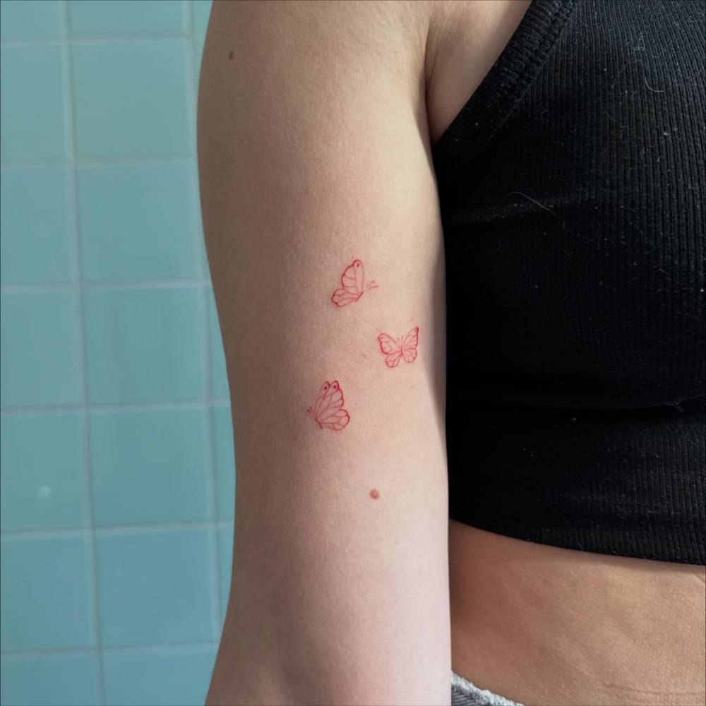 Red butterflies tattoo in fine line style located on the bicep.
