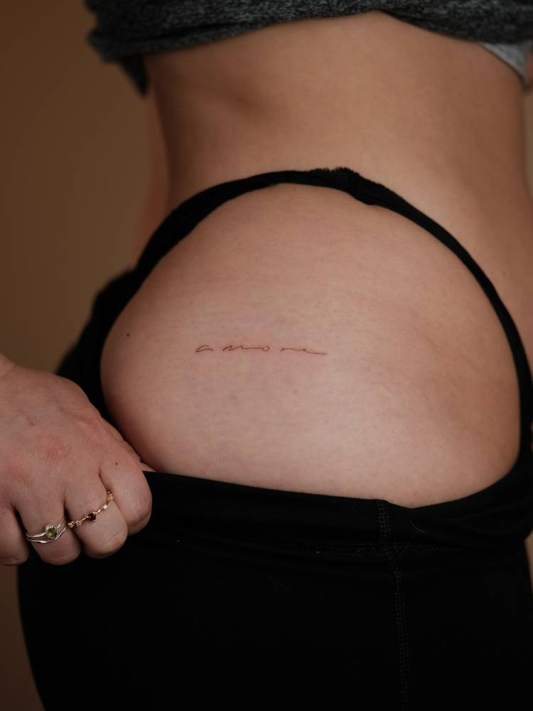 Handwritten font word "amore" tattooed on the hip.