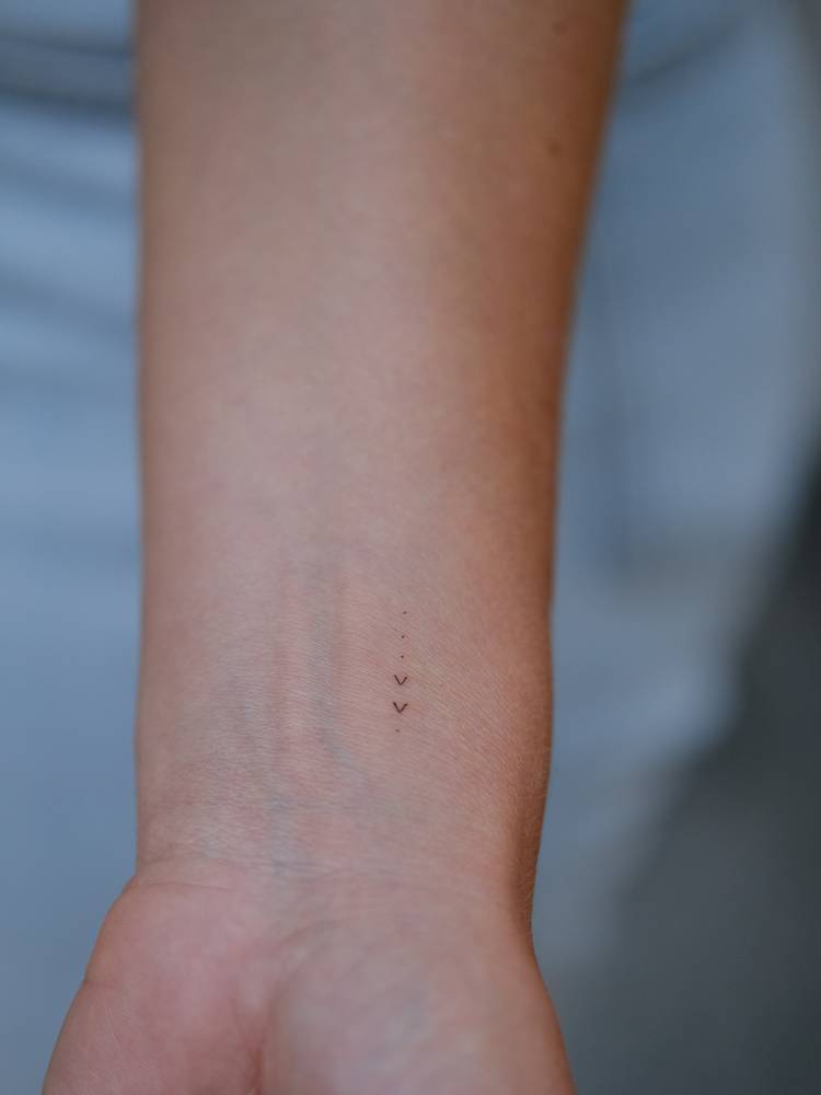Tiny minimalistic hearts and dots tattoo placed on the wrist.