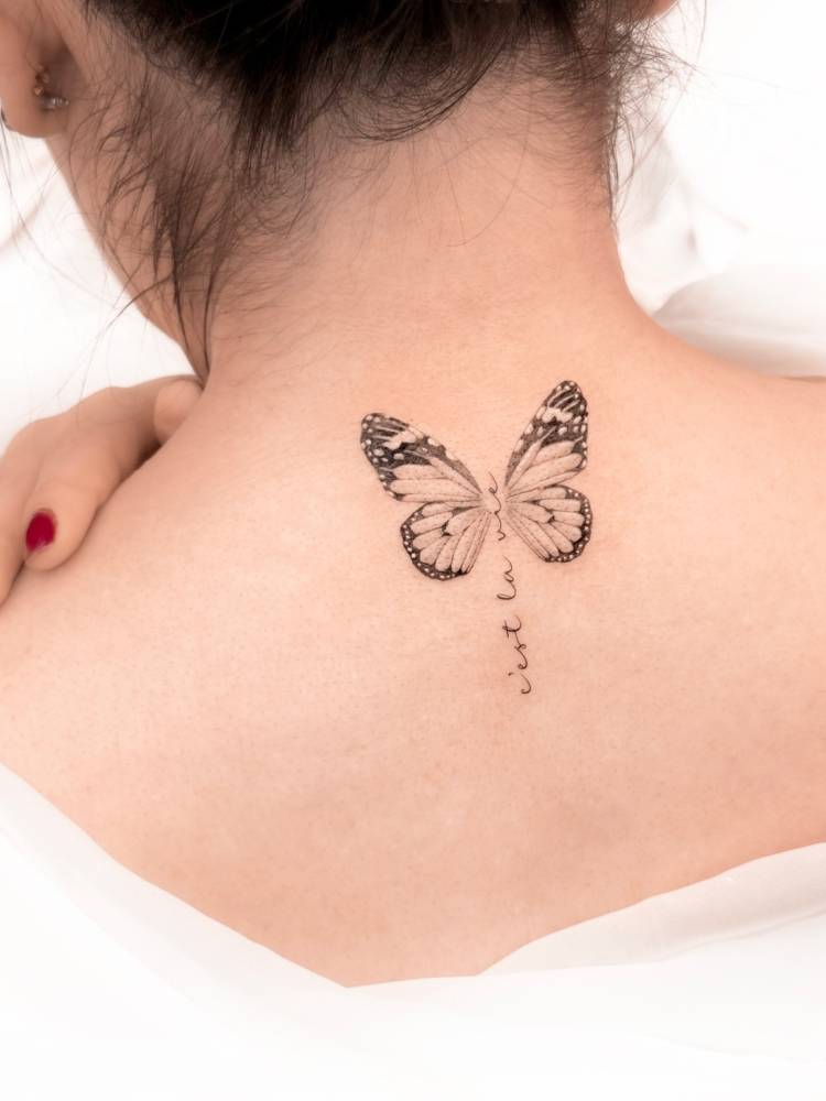 "C'est la vie" and butterfly tattoo located on the upper back.