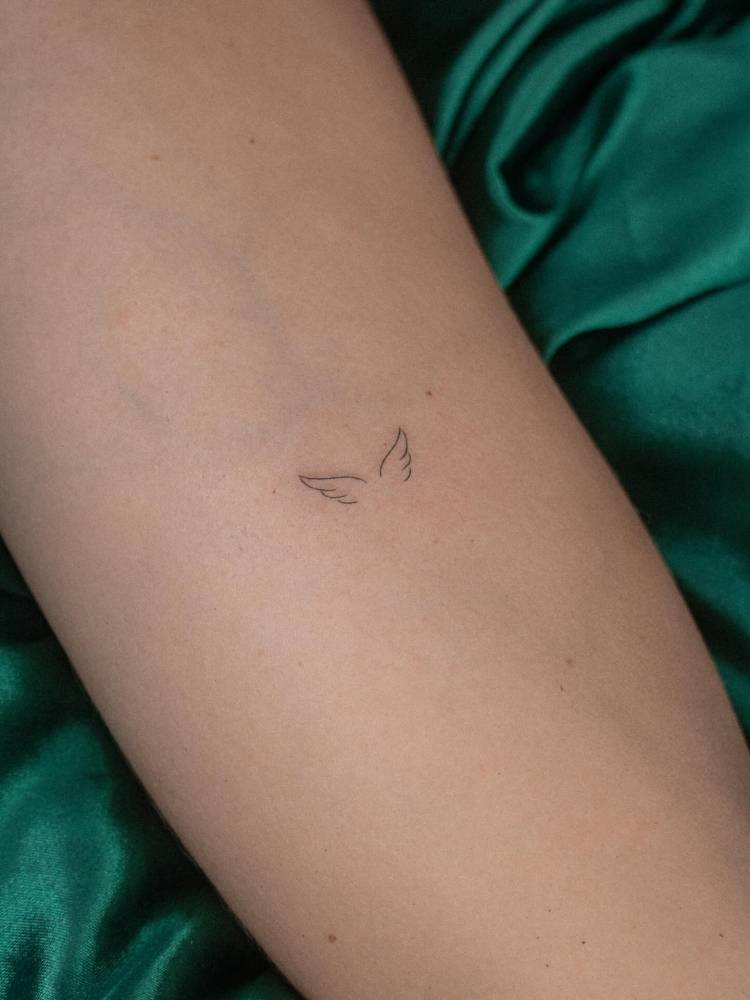 Minimalistic style angel wings tattoo located on the inner forearm.