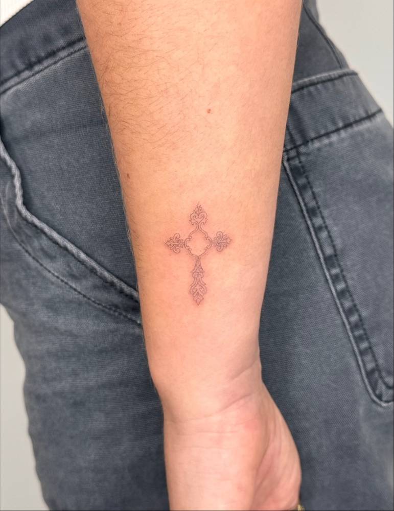 Fine line style cross tattoo located on the wrist.