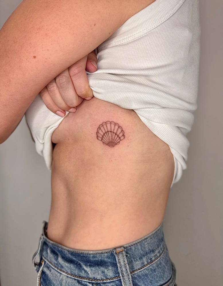Fine line style scallop shell tattoo done on the rib.