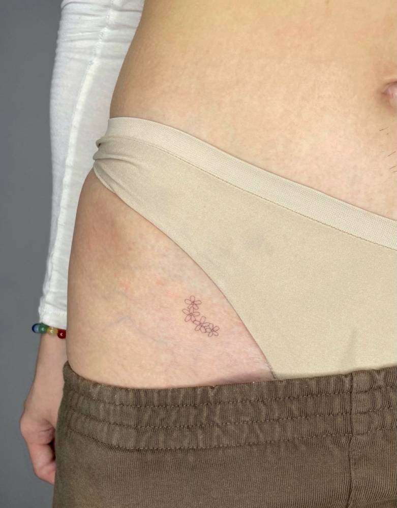 Tiny minimalistic flowers tattooed on the pelvis.