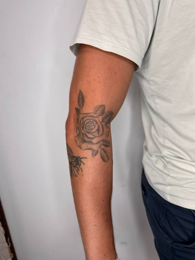 Rose head tattoo in illustrative style done on the elbow.
