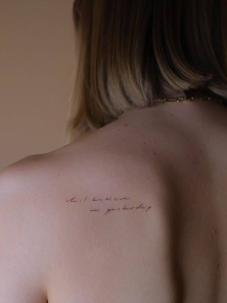 Lettering tattoo that says "oh, I believe in yesterday" done on the shoulder blade.