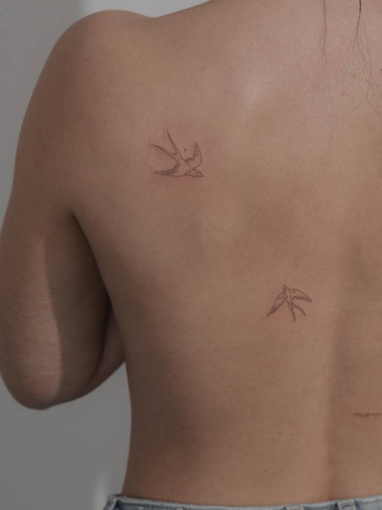 Fine line style swallow couple tattoo located on the back.