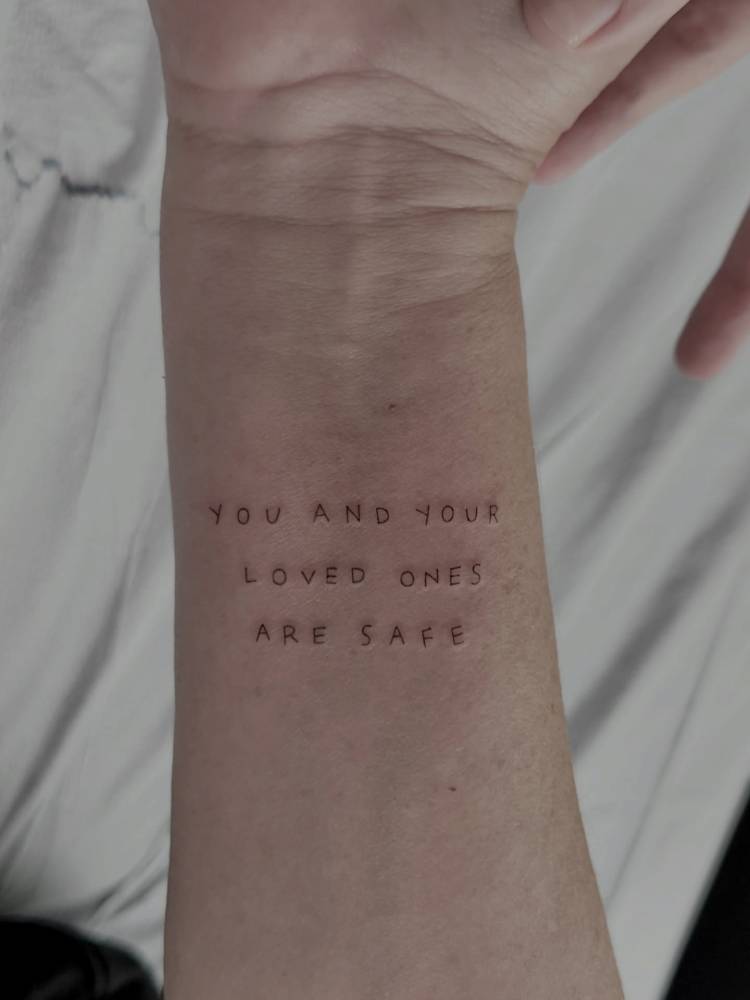 "You and your loved ones are safe" lettering tattoo located on the wrist.