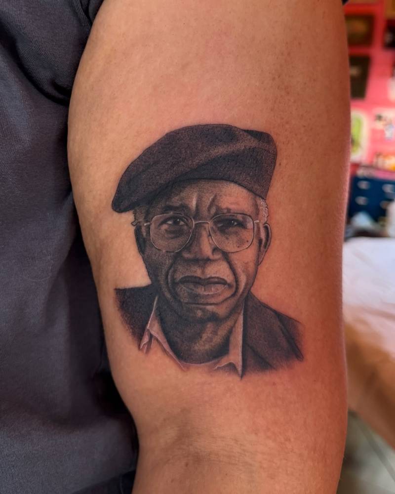 Chinua Achebe portrait tattoo located on the upper arm, black and grey style.