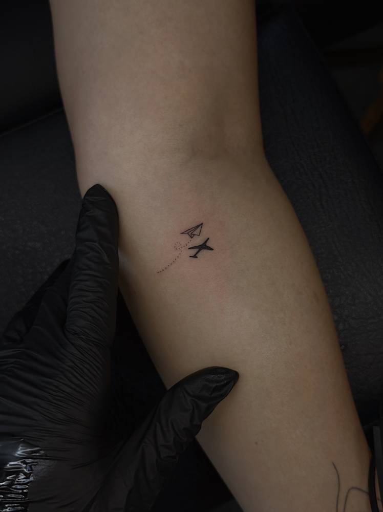 Paper plane tattoo located on the inner forearm, minimalistic style.