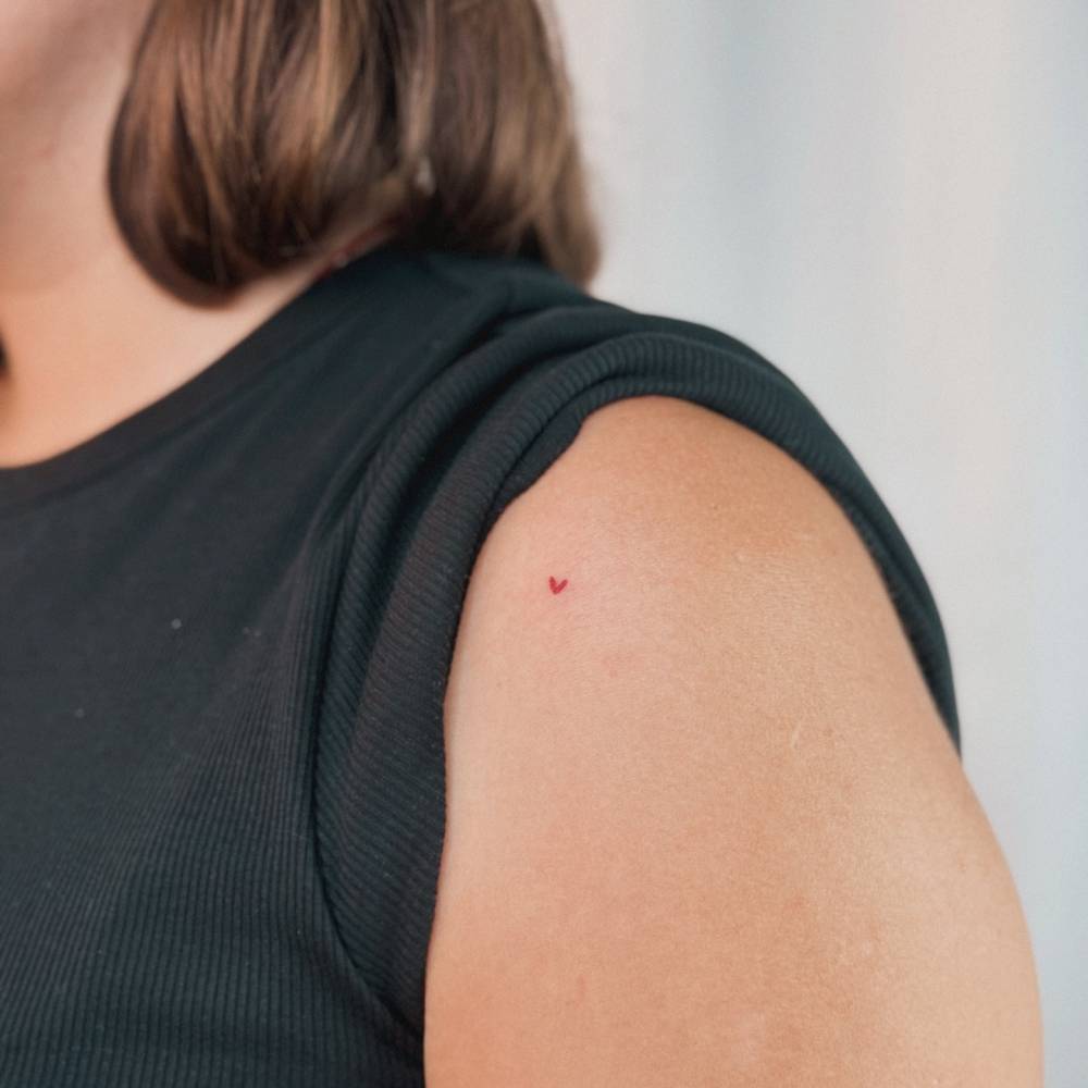 Red heart tattoo placed on the shoulder, done in minimalistic style.