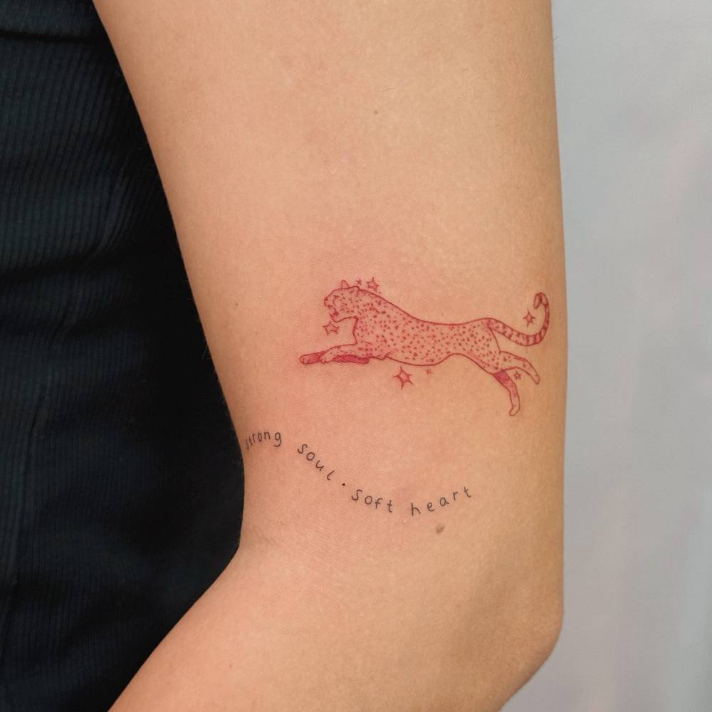 Red leopard tattoo in illustrative style located on the upper arm.