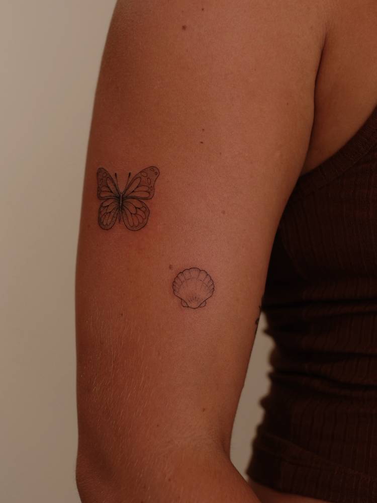 Butterfly and scallop shell tattoos located on the upper arm.