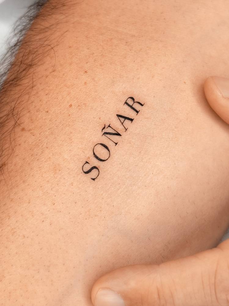 Lettering tattoo of the word "soñar" in serif font located on the inner forearm.